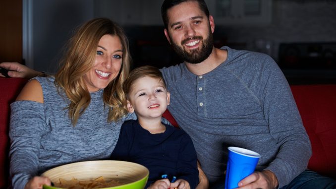 Family Sitting On Sofa Watching Television Together